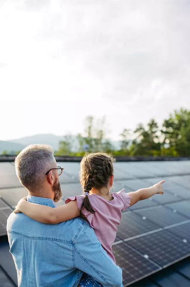 Rückansicht des Vaters mit Mädchen auf dem Dach mit Sonnenkollektoren
